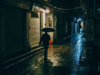 Rear view of man walking on wet street at night