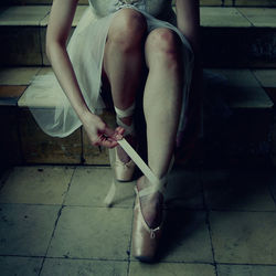 Low section of ballet dancer wearing shoe while sitting on staircase