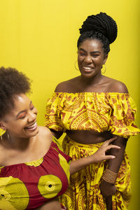 Portrait of two women against yellow background. one of them is pregnant and sitting. 