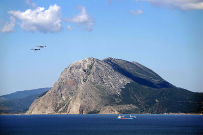 Airplanes flying over sea against sky and cargo ship going on the opposite direction. 