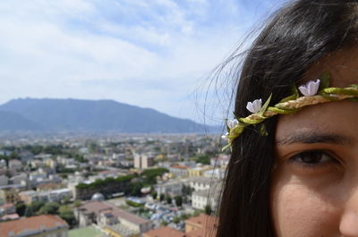 Cropped portrait of woman wearing artificial flowers against cityscape