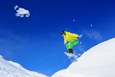 Full length of man snowboarding on snowcapped mountain against blue sky