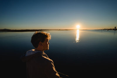 Side view of man standing in lake against sky during sunset