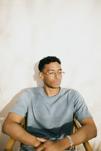 Young man with eyes closed sitting on chair under sunlight at backyard