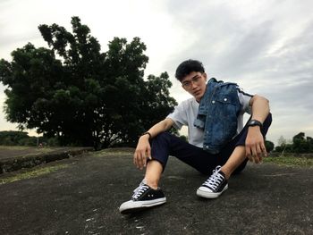 Young man sitting in park against sky