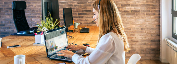 Woman with headset typing in laptop in customer help service