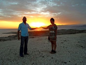 Portrait of couple standing on sand at beach during sunset