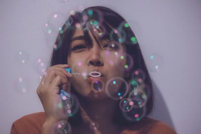 Portrait of woman blowing bubbles against white wall