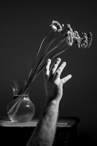 Close-up of hand holding flower vase against black background