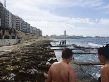 Rear view of friends at beach by buildings against sky