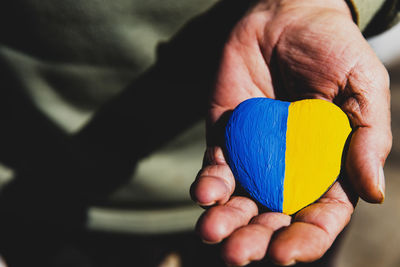 Senior man or soldier hands holding heart shape stone painted with ukraine national flag colors