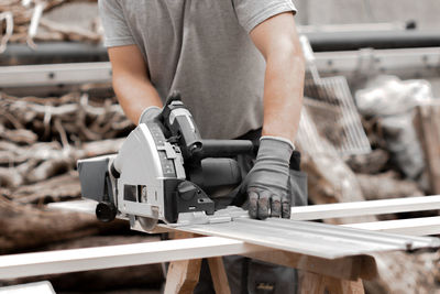 A young man is sawing a board with an electric saw.