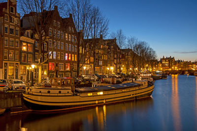 Boats moored on canal by illuminated buildings in city at night