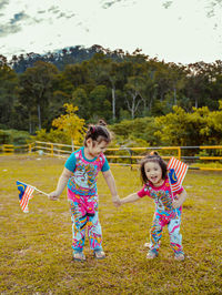 Full length cute sisters holding flag standing on grass at park