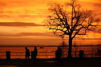 Silhouette people standing on beach against orange sky