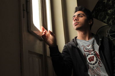 Thoughtful young man looking through window