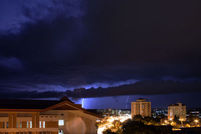Illuminated buildings against cloudy sky at night