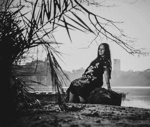 Pregnant woman looking away while sitting on fallen tree against sky