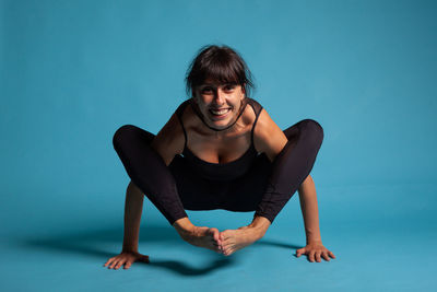 Portrait of young woman sitting against blue background