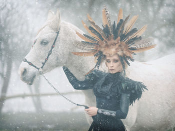 Young woman in costume with horse standing outdoors during winter