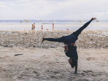 Young man doing handstand at sandy beach