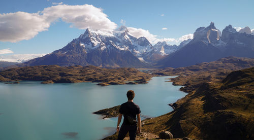 Rear view of man standing on mountain while looking at sea against sky