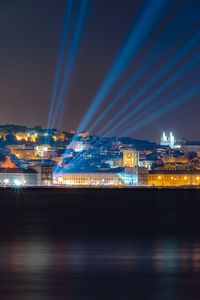 Illuminated buildings by river against sky at night