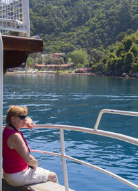 Woman looking at river while sitting on jetty against mountains