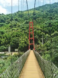 Footbridge amidst trees in forest against sky