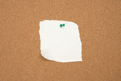 Torn white blank white sheet of paper affixed with a plastic button on a brown cork board, c