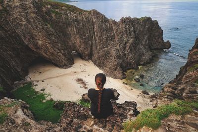 Rear view of woman sitting on rock at beach