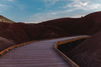 Boardwalk leading towards mountains against cloudy sky
