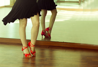 Low section of woman in high heels on hardwood floor with reflection in mirror