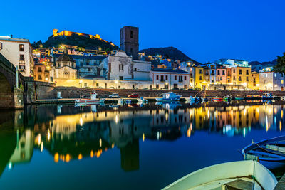 River by illuminated buildings against blue sky