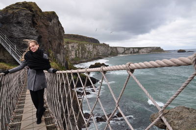 Full length portrait of woman standing on footbridge at coastline