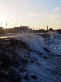 Sea waves splashing on shore against sky during sunset