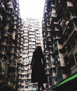 Rear view of woman standing amidst buildings in city