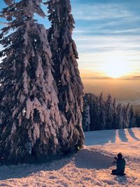 Silhouette young woman sitting on snow covered mountain against sky during sunset