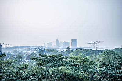 Trees and buildings in city against clear sky