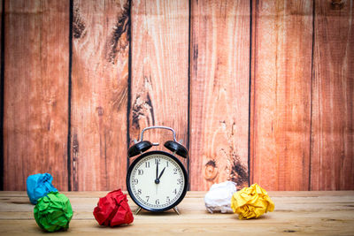 Close-up of alarm clock with colorful crumpled papers on wooden table against wall