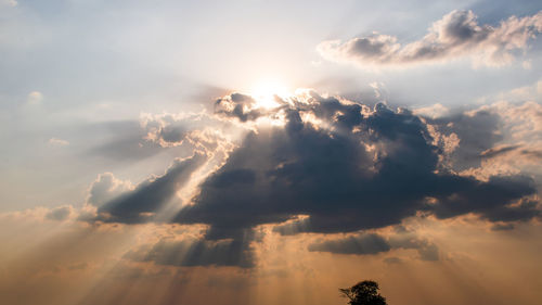 Low angle view of sunlight streaming through clouds