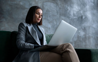 Young woman using laptop while sitting on sofa at home