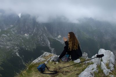 Person on rocks by mountains during foggy weather