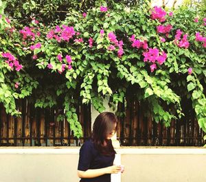 Young woman walking against bougainvillea on fence