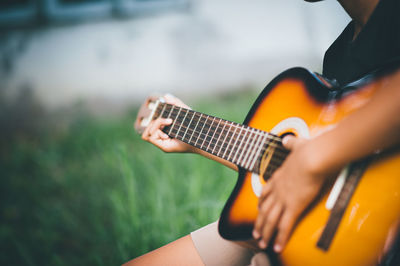 Cropped hand of person playing guitar over field