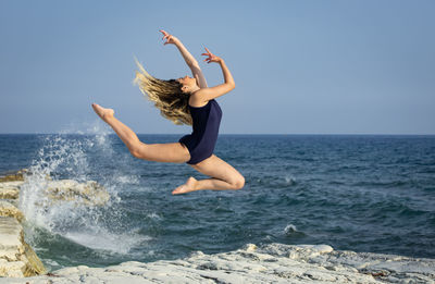 Young woman dancing outdoors on a rocky coast by the ocean