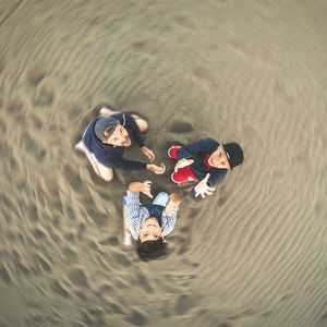 High angle portrait of father and sons sitting on sand at beach