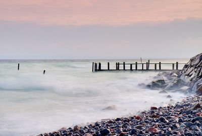 Abandoned wooden wharf in sea within blue pink color of sky, blur waves on water level.