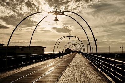 Railroad tracks by street against sky during sunset