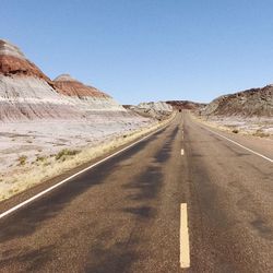 Road leading towards mountains against clear sky